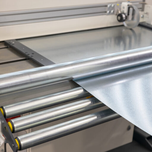 Close-up view of a metal sheet processing machine with a rolling system used in modern manufacturing. The image captures the precision and automation involved in metalworking and industrial production, showcasing the machinery used to handle and cut metal sheets in high-tech factories. Ideal for themes related to manufacturing, metalworking, automation, and industrial engineering.